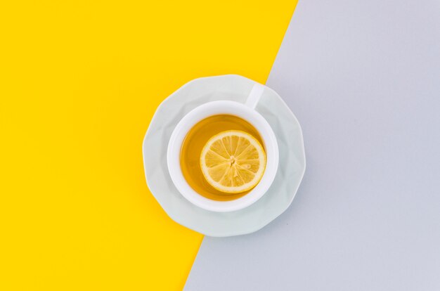 Une vue de dessus de la tasse de thé au citron et sa soucoupe sur fond blanc et jaune