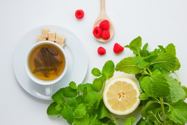 Vue de dessus une tasse de thé au citron, sucre, feuilles de menthe, framboise sur une surface blanche. horizontal