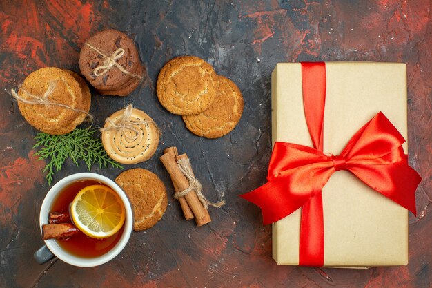 Vue de dessus tasse de thé bâtons de cannelle différents biscuits attachés avec une corde présente la main sur une table rouge foncé