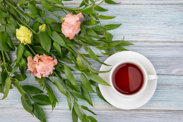 Vue de dessus d'une tasse de thé avec de belles fleurs et feuilles sur gris