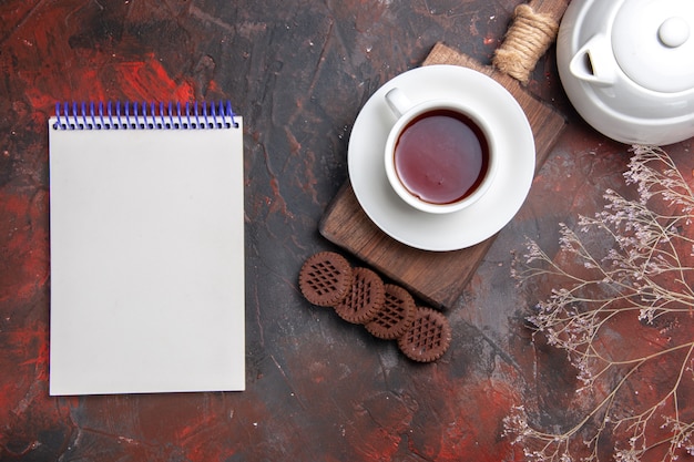 Vue de dessus tasse de thé avec des biscuits sur un bureau sombre