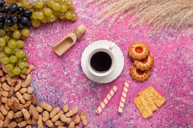 Vue de dessus tasse de thé avec des biscuits, des craquelins, des arachides et des raisins frais sur le bureau rose biscuit fruits noix couleur crisp