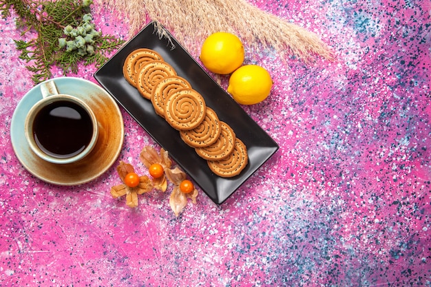 Vue de dessus tasse de thé avec des biscuits et du citron sur le bureau rose.