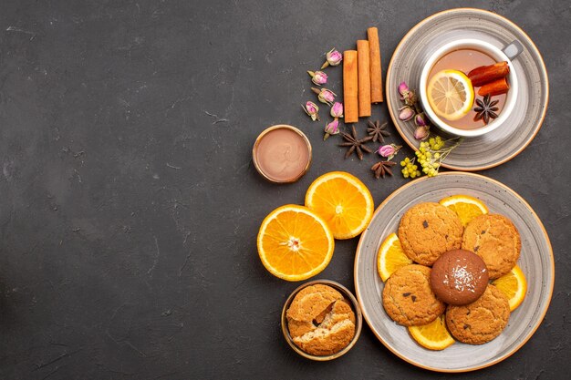 Vue de dessus tasse de thé avec des biscuits et des tranches d'oranges fraîches sur la surface sombre biscuit aux fruits au thé sucré