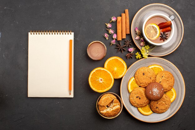 Vue de dessus tasse de thé avec des biscuits et des tranches d'oranges fraîches sur une surface sombre biscuits aux fruits au thé sucré