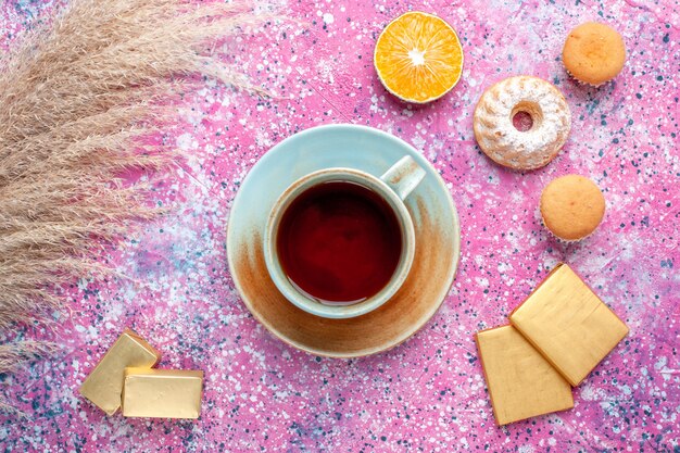 Vue de dessus de la tasse de thé avec des bonbons au chocolat et des gâteaux sur la surface rose