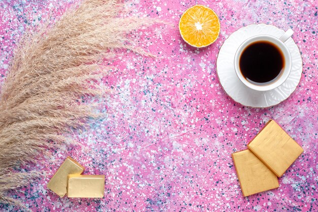 Vue de dessus de la tasse de thé avec des bonbons au chocolat sur une surface rose