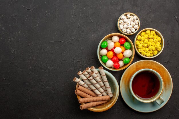 Vue de dessus tasse de thé avec des bonbons et des biscuits sur un espace sombre