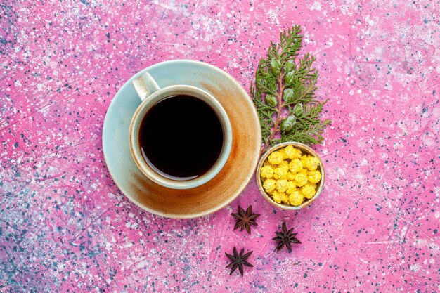 Vue de dessus tasse de thé avec des bonbons jaunes sur un bureau rose