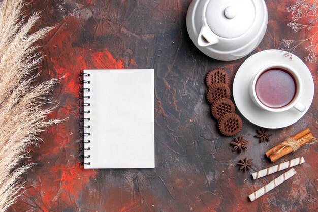 Vue de dessus tasse de thé avec bouilloire et biscuits sur un bureau sombre