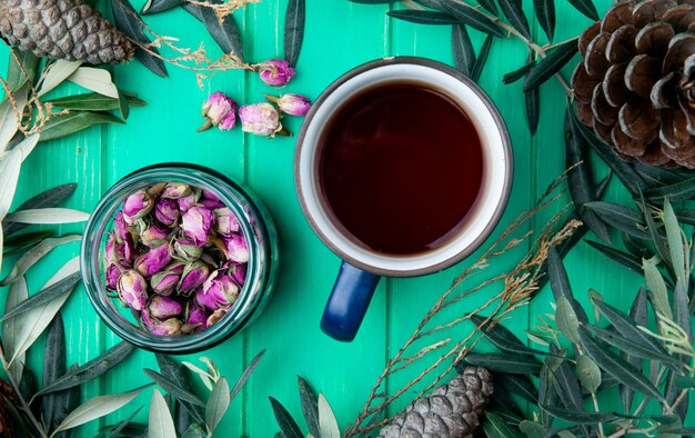 Vue de dessus d'une tasse de thé avec des boutons de rose de thé sec dans un bocal en verre sur bois vert