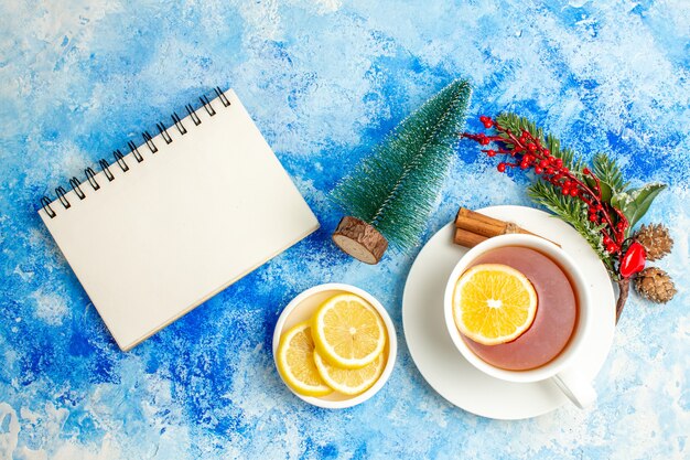 Photo gratuite vue de dessus tasse de thé branche d'arbre de noël citrons coupés sur le bloc-notes de la soucoupe sur la table bleue