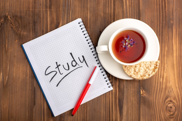 Vue de dessus tasse de thé avec cahier et crayon sur un bureau marron