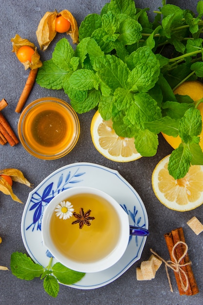 Vue de dessus une tasse de thé à la camomille avec des feuilles de menthe, citron, miel, cannelle sèche.