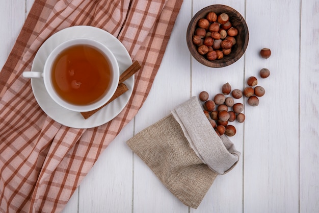 Vue de dessus tasse de thé à la cannelle sur une serviette et noisettes dans un sac de jute sur fond gris