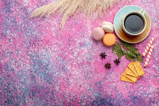 Vue de dessus tasse de thé avec des craquelins et des macarons sur une surface rose clair