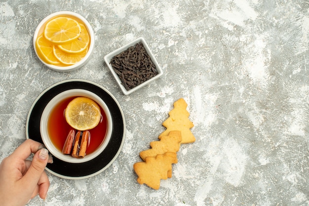 Vue de dessus une tasse de thé dans un bol de biscuits à la main de femme avec des tranches de chocolat et de citron sur l'espace libre de surface grise