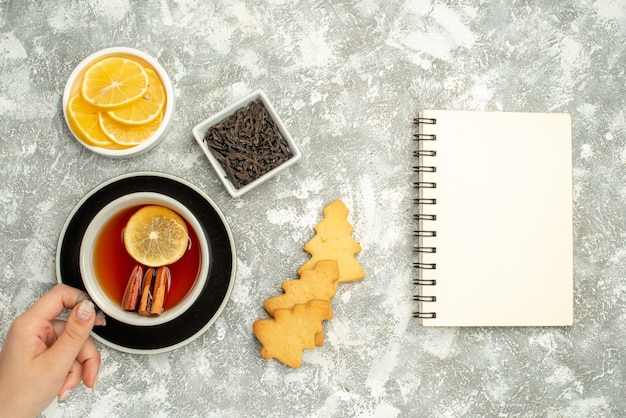 Vue de dessus une tasse de thé dans un bol de biscuits à la main femme avec des tranches de chocolat et de citron sur une surface grise