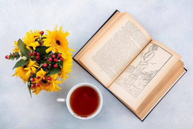Vue de dessus de la tasse de thé et de fleurs avec livre ouvert sur blanc