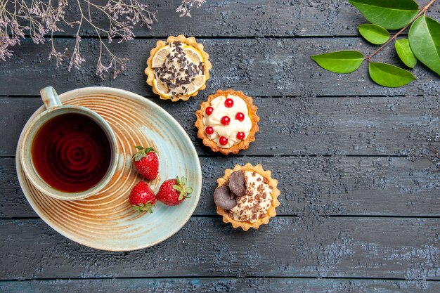 Vue de dessus une tasse de thé et de fraises sur les feuilles de tartes soucoupe et branche de fleurs séchées sur table en bois foncé