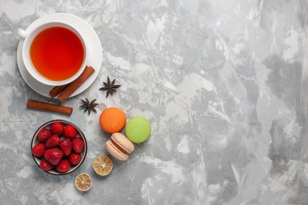 Vue de dessus tasse de thé avec des fraises fraîches et des macarons français sur une surface blanche