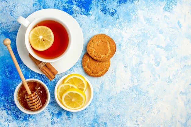 Vue de dessus tasse de thé miel dans un bol biscuits tranches de citron sur l'espace libre de la table bleue