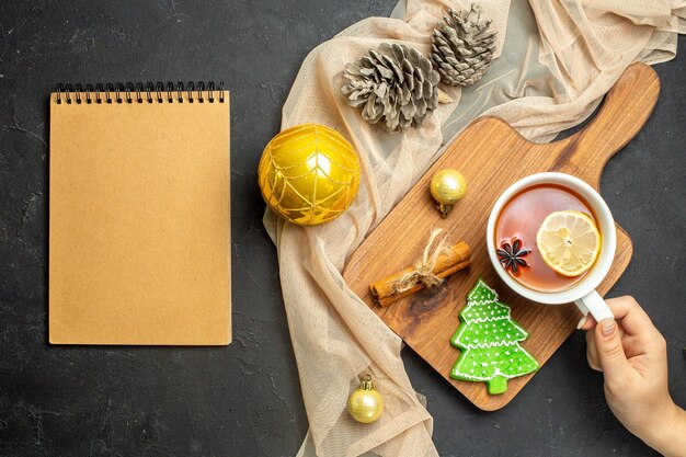 Vue de dessus d'une tasse de thé noir avec des accessoires de décoration de nouvel an au citron et à la cannelle sur une planche à découper en bois sur un cahier publicitaire de serviette de couleur nude