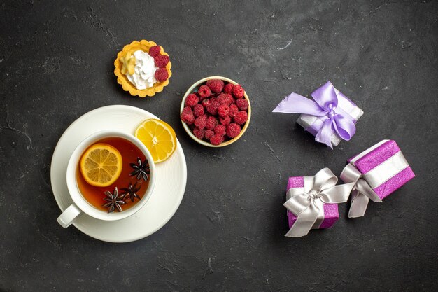 Vue de dessus d'une tasse de thé noir au citron servie avec une framboise au chocolat et des cadeaux sur fond sombre