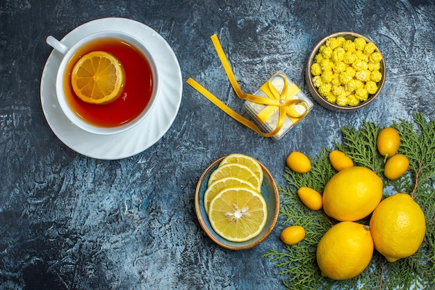 Vue de dessus d'une tasse de thé noir avec des bonbons au citron et une boîte-cadeau de la moitié de la collection entière d'agrumes sur des branches de sapin sur fond sombre