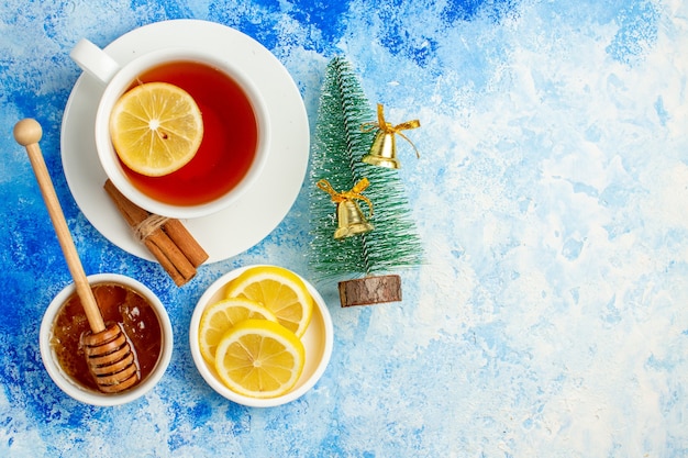 Vue de dessus tasse de thé petit arbre de Noël tranches de citron miel et bâton de miel dans un bol sur l'espace libre de la table bleue