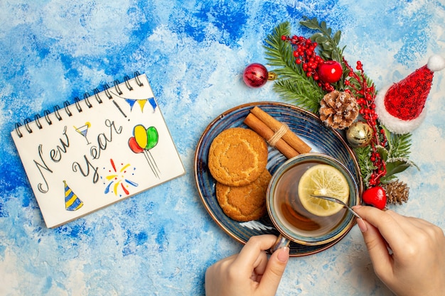 Vue de dessus tasse de thé tranches de citron bâtons de cannelle biscuits en soucoupe nouvel an écrit sur le bloc-notes sur la table bleue