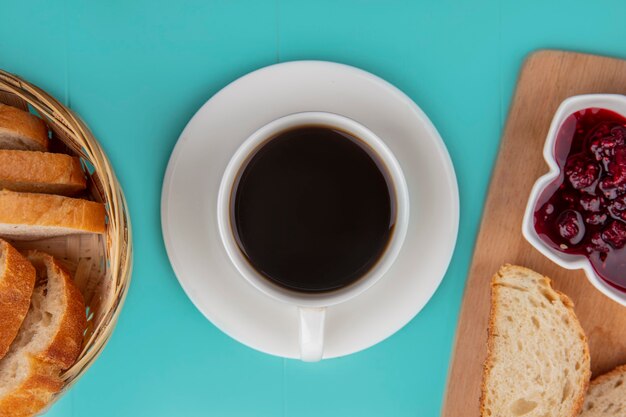 Vue de dessus de la tasse de thé avec des tranches de pain et de la confiture de framboises sur une planche à découper sur fond bleu