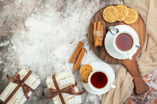 Vue de dessus des tasses de thé avec des biscuits sucrés et des cadeaux sur fond clair pause gâteau au sucre couleur de la tarte