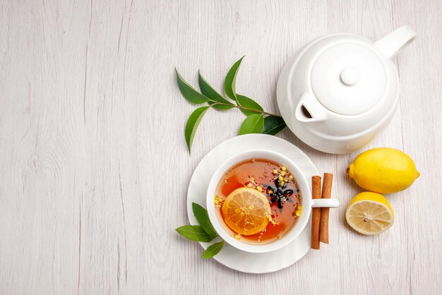 Vue de dessus thé et cannelle une tasse de tisane bâtons de cannelle sur la soucoupe théière au citron et feuilles sur le tableau blanc