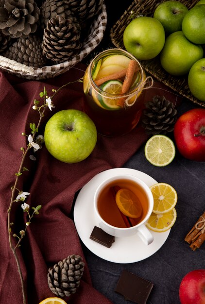 Vue de dessus thé tasse de thé au citron et à la cannelle thé glacé au citron vert citron à la cannelle chocolat noir vert pommes rouges fleurs blanches et pommes de pin