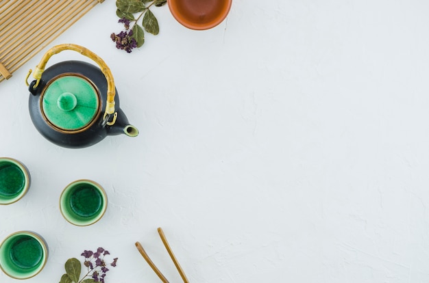 Photo gratuite une vue de dessus de la théière à base de plantes vertes en céramique et des tasses avec des herbes isolées sur fond blanc