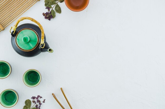 Une vue de dessus de la théière à base de plantes vertes en céramique et des tasses avec des herbes isolées sur fond blanc