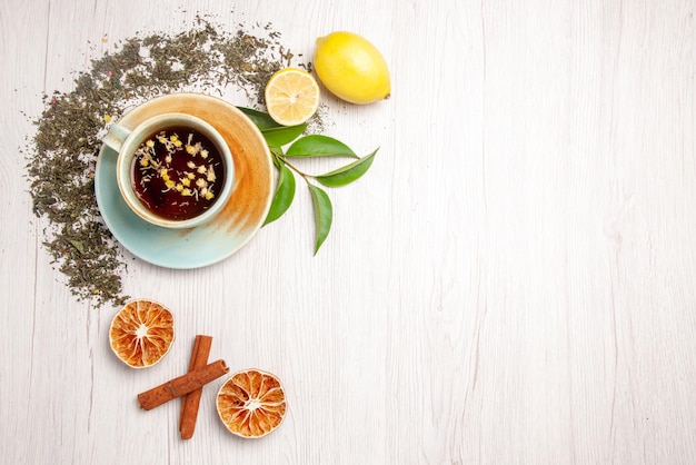 Vue de dessus tisane tasse blanche de tisane à côté des herbes citron cannelle sur le tableau blanc