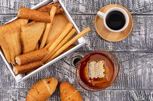 Vue de dessus des toasts avec des craquelins dans une caisse avec du miel et du café sur une surface blanche horizontale