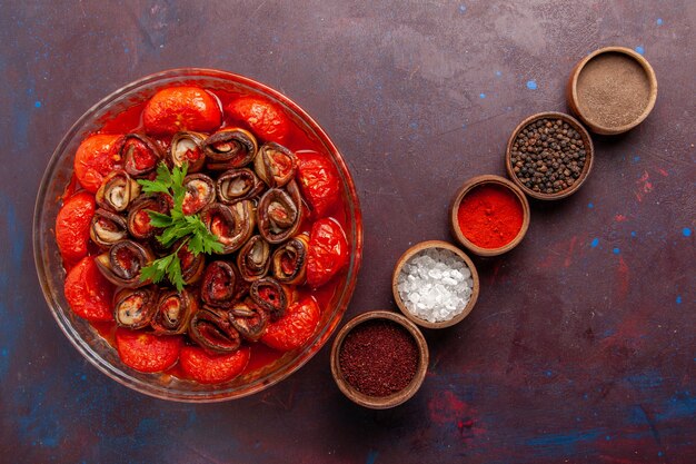 Vue de dessus tomates et aubergines repas de légumes cuits roulés et cuits avec des assaisonnements sur le bureau sombre