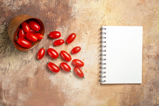 Vue de dessus des tomates cerises dispersées dans un bol d'un cahier sur fond ambre