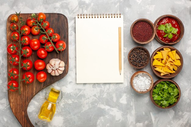 Vue de dessus tomates cerises fraîches avec assaisonnements et bloc-notes sur une surface blanche