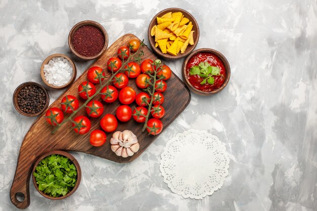 Vue de dessus tomates cerises fraîches avec assaisonnements et légumes verts sur une surface blanche