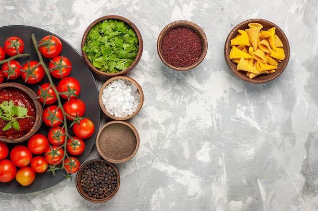 Vue de dessus tomates cerises fraîches à l'intérieur de la plaque avec différents assaisonnements sur un bureau blanc