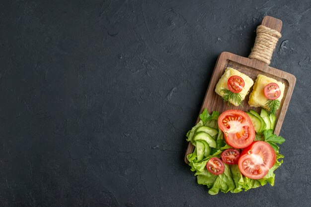 Vue de dessus des tomates et concombres frais coupés sur planche de bois sur le côté gauche sur surface noire