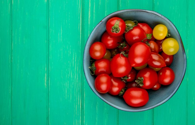 Vue de dessus des tomates dans un bol sur le côté droit et la surface verte avec copie espace