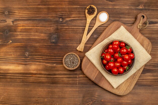 Vue de dessus des tomates fraîches sur un bol marron sur une planche à découper et des épices dans des cuillères de poivre sur une planche de bois