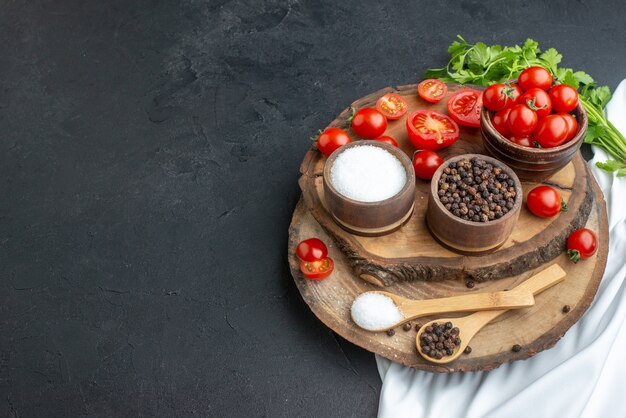 Vue de dessus des tomates fraîches et des épices dans des bols cuillères sur planche de bois sur le côté gauche sur la surface noire