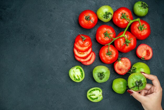 Vue de dessus tomates hachées branche de tomate tomate verte fraîche dans la main féminine sur tableau noir