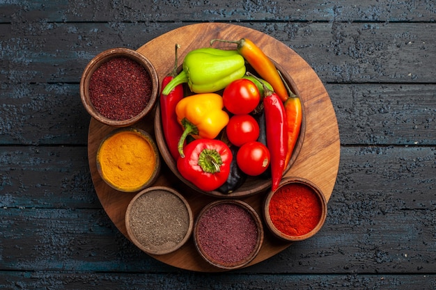 Vue de dessus tomates légumes frais et poivrons avec assaisonnements sur un bureau sombre